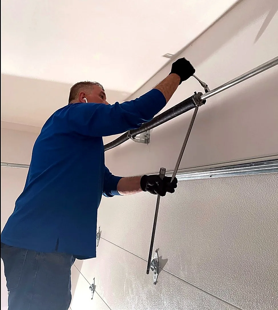 Technician adjusting garage door torsion spring hardware